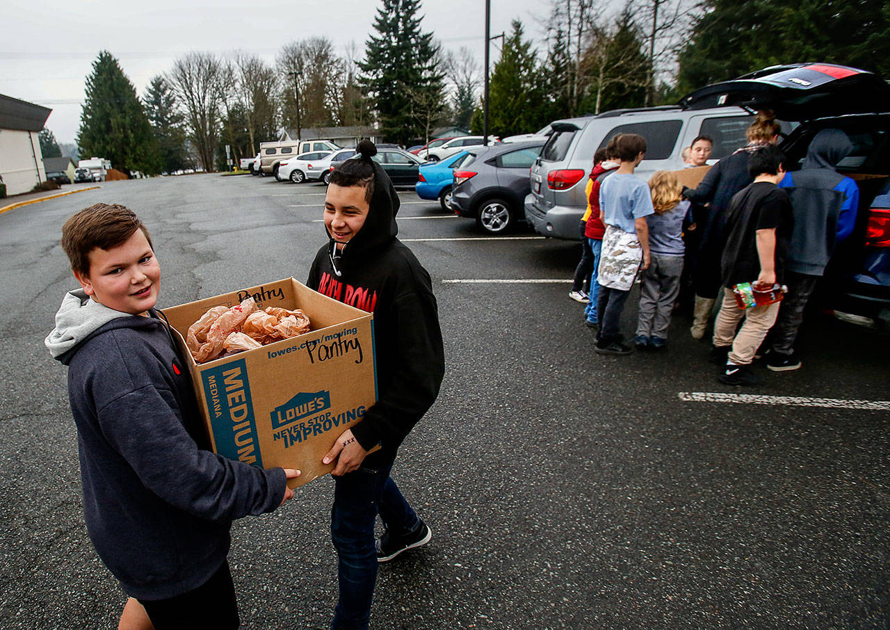 Ryder Dow, 11, walks backward with his end of a box of food while Angel Lopez, 12, helps carry the load to their Social Skills classroom at North Lake Middle School. Other students help their teacher, Ange Kendall, unload food that will soon be delivered to the Lake Stevens Community Food Bank. (Dan Bates / The Herald)