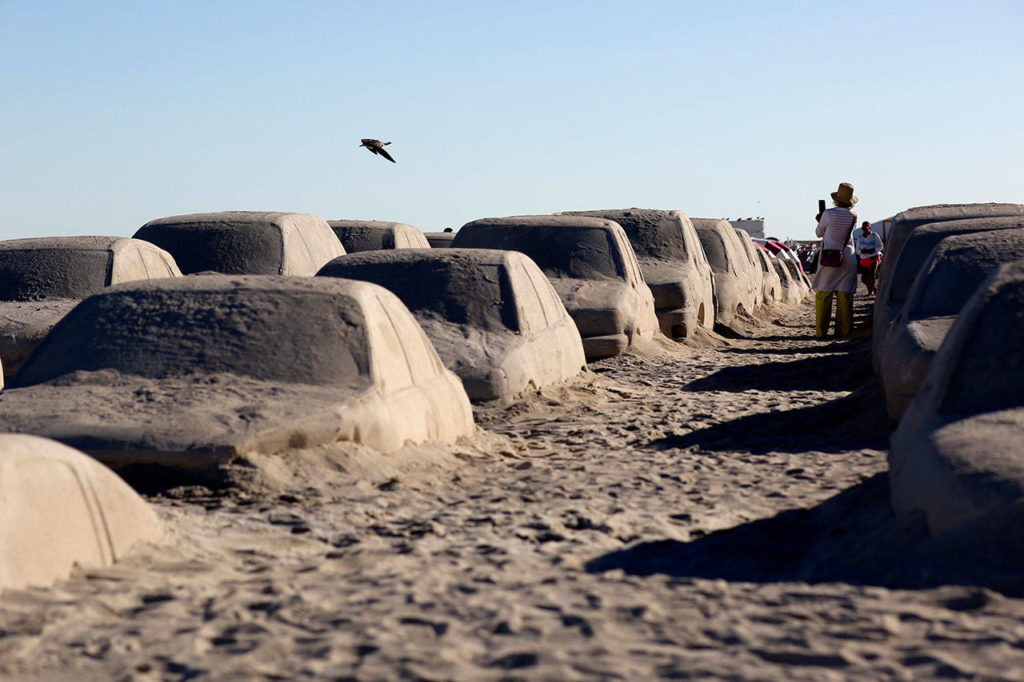 People walk among cars sculpted in sand stuck in a traffic jam, titled Order of Importance by artist Leandro Erlich, as part of Miami Art Week, Tuesday, Dec. 3, 2019, in Miami Beach, Fla. Erlich was commissioned by the city of Miami Beach to create the work, which was unveiled during Art Basel Miami. (AP Photo/Lynne Sladky)
