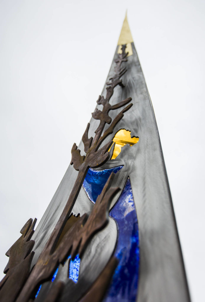 Monroe’s new sculpture features an outline of jagged mountain peaks, river rocks and blue glass (to represent the Snohomish and Skykomish rivers flowing nearby) and an alpine tree on its front. (Olivia Vanni / The Herald)
