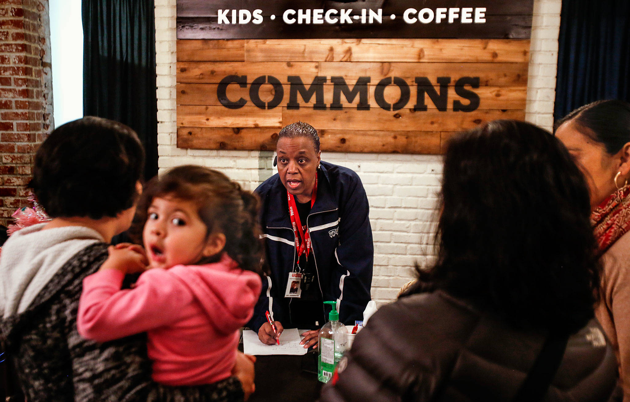 At Toys for Tots, located in Everett’s Foundation Church, Mary Butler (facing) checks in families and asks questions that will help her help them. One client holds a small child as she waits while Butler and other volunteers get ready to choose just the right gifts from a huge selection stored out of sight. (Dan Bates / The Herald)