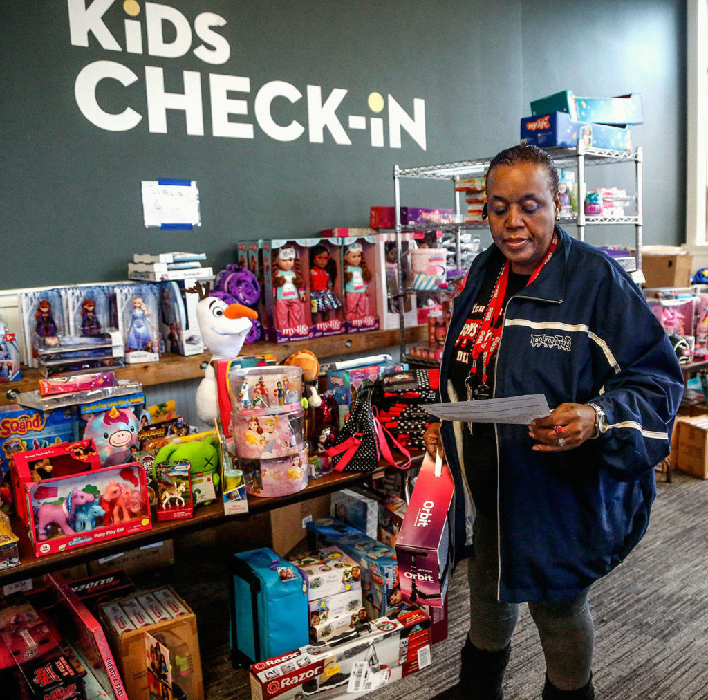 Mary Butler scans a profile she created of a child’s favorite things and searches the Toys for Tots distribution room at Everett’s Foundation Church for just the right match. (Dan Bates / The Herald)
