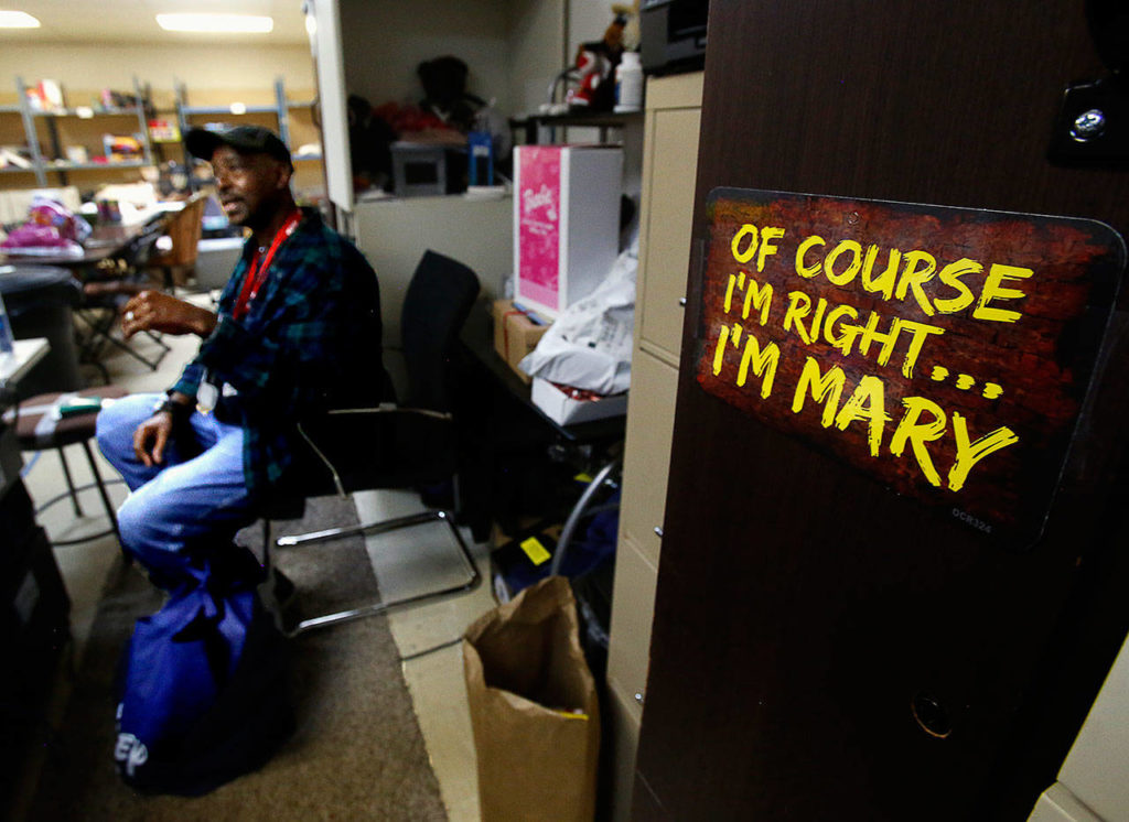 King Butler, the husband of Toys for Tots coordinator Mary Butler, helps out on the lower level of Foundation Church on Thursday as his wife serves families needing gifts for their children. A funny sign there bears his wife’s name. (Dan Bates / The Herald)
