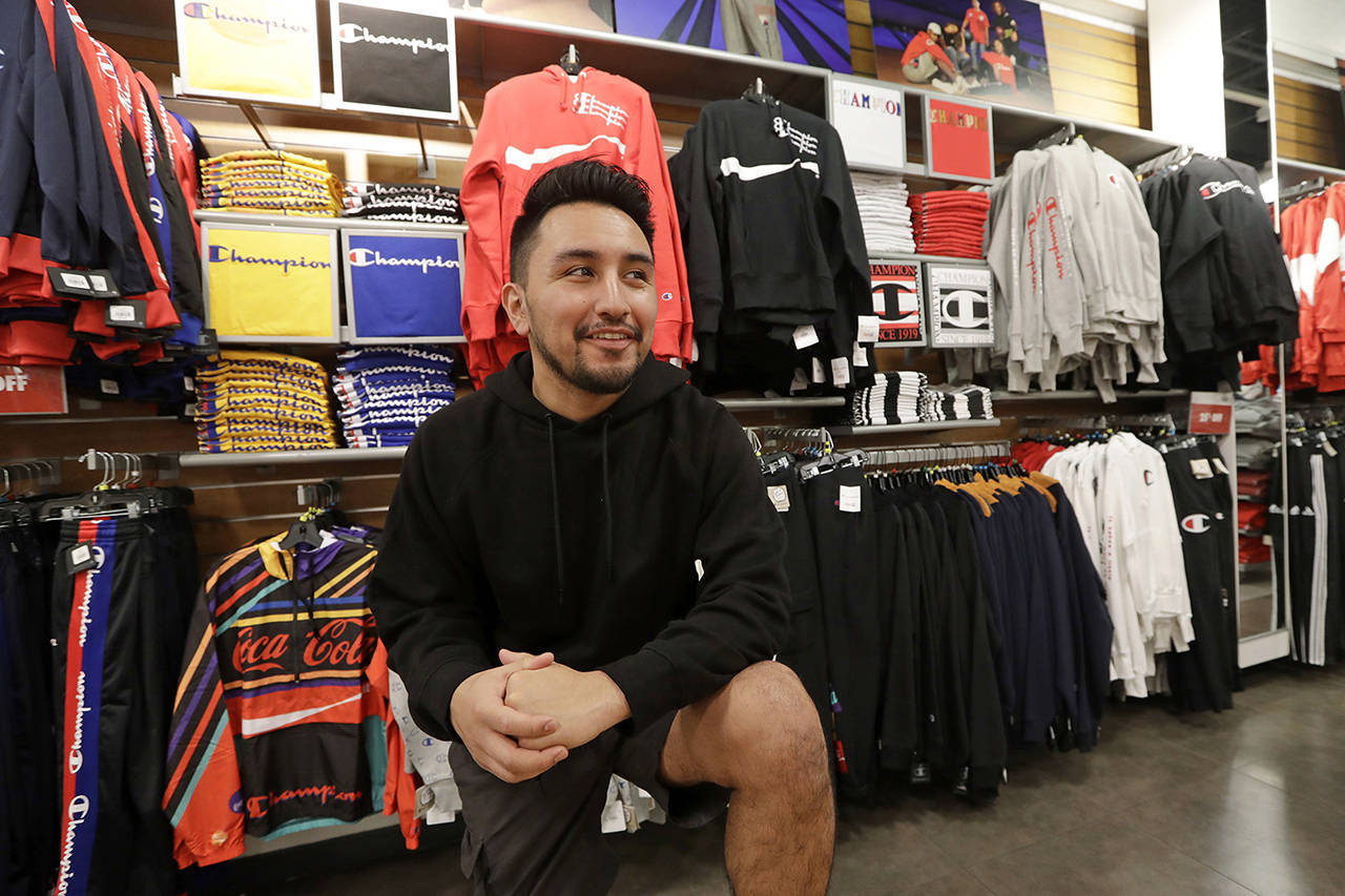 Victor Duran, a co-manager of a sports apparel store at the Southcenter mall, south of Seattle, poses for a photo at the store Dec. 11 in Tukwila. Duran, 23, said he makes about $52,000 a year and doesn’t get overtime, but is required to work at least 45 hours per week, and up to 60 during the holidays. (AP Photo/Elaine Thompson)