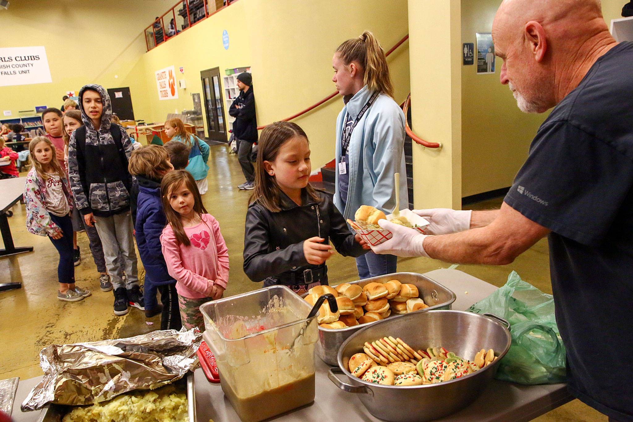 Robert Gamache (right), a volunteer with Angel Resource Connection, hands over a dish of food to some of the more than 100 students who were served hot meals at the Granite Falls Boys & Girls Club. (Kevin Clark / The Herald)