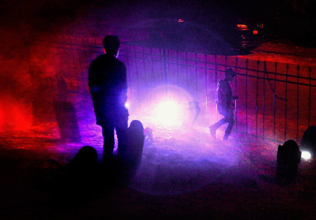 Daxton Ackert, 14, and his 11-year-old brother Kruz check out the special Halloween lighting near the graveyard fence outside their home in Everett’s South Forest Park neighborhood. (Dan Bates / The Herald)
