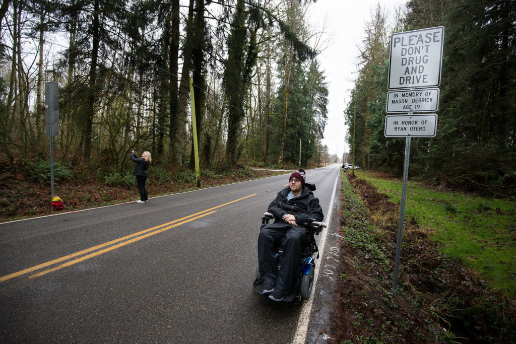 Caprice Deguzman takes photos of signs dedicated to her son, and crash survivor, Ryan Otero, after the signs were unveiled in the 27000 block of 15th Avenue NE on Friday in Arlington. Otero is paralyzed because of the wreck, which cost Mason Derrick his life 10 years ago. (Andy Bronson / The Herald)
