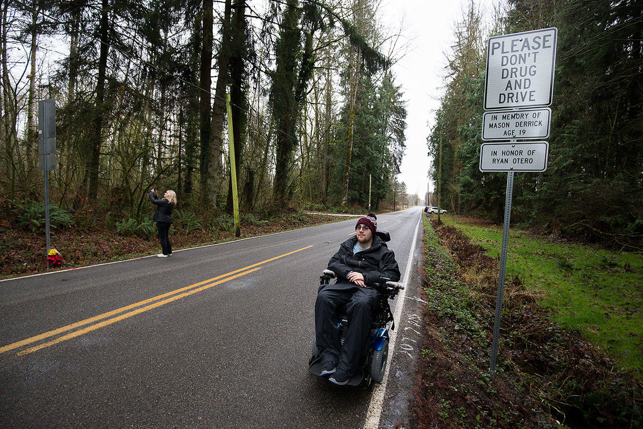 Caprice Deguzman takes photos of signs dedicated to her son, and crash survivor, Ryan Otero, after the signs were unveiled in the 27000 block of 15th Avenue NE on Friday in Arlington. Otero is paralyzed because of the wreck, which cost Mason Derrick his life 10 years ago. (Andy Bronson / The Herald)