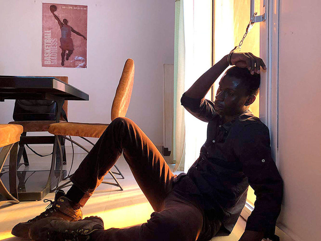 A young detective played by Amadou Mbow in “Atlantics” finds himself cuffed to a sliding glass door while investigating strange events in Dakar. (Frakas Productions)
