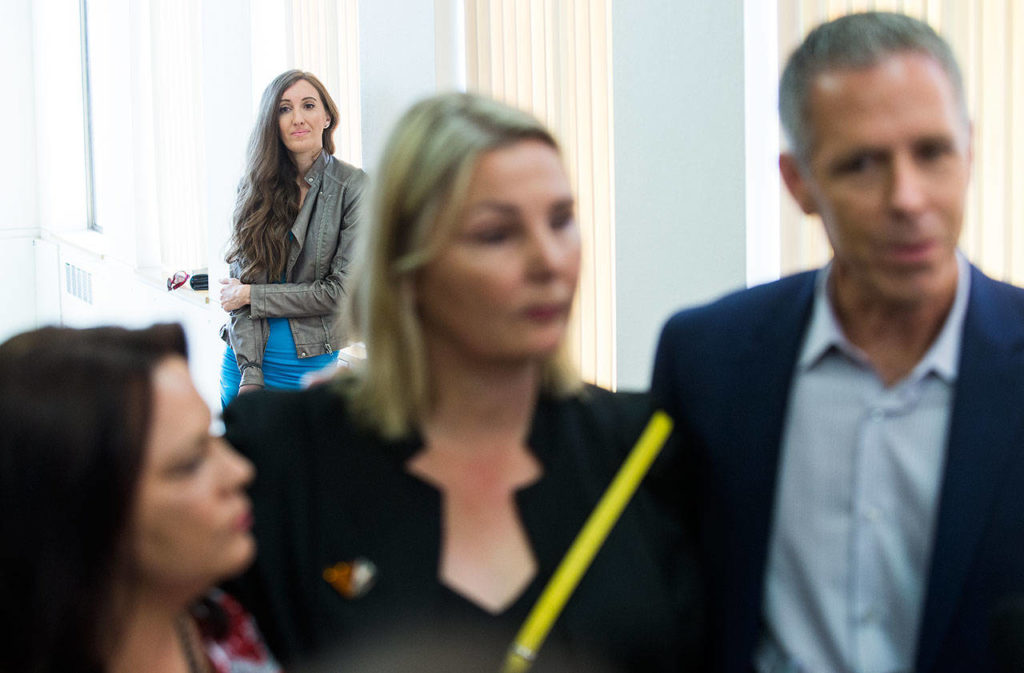 Chelsea Rustad watches from a hallway as John Van Cuylenborg (right), Kelly Cook and Laura Baanstra talk to the media after William Talbott II is sentenced to life with out parole at the Snohomish County Courthouse on July 24 in Everett. Rustad’s AncestryDNA test led to the arrest of Talbott, later convicted of killing of Tanya Van Cuylenborg and Jay Cook. (Andy Bronson / The Herald)
