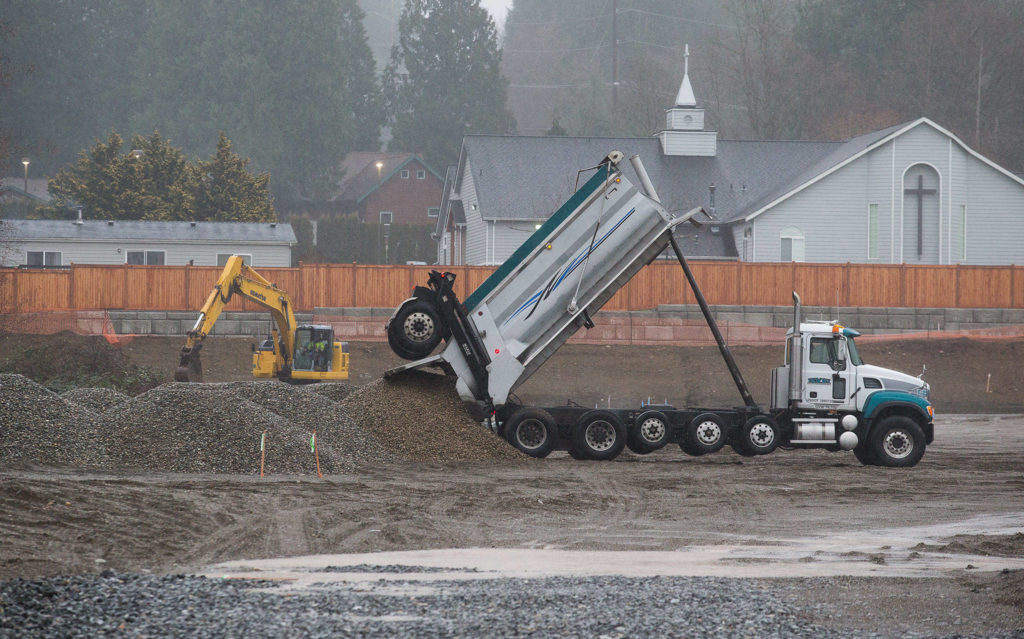A dump trunk drops off a load of gravel as an excavator moves dirt on Monday, preparing land for new apartments at 67th Ave. NE. (Andy Bronson / The Herald)
