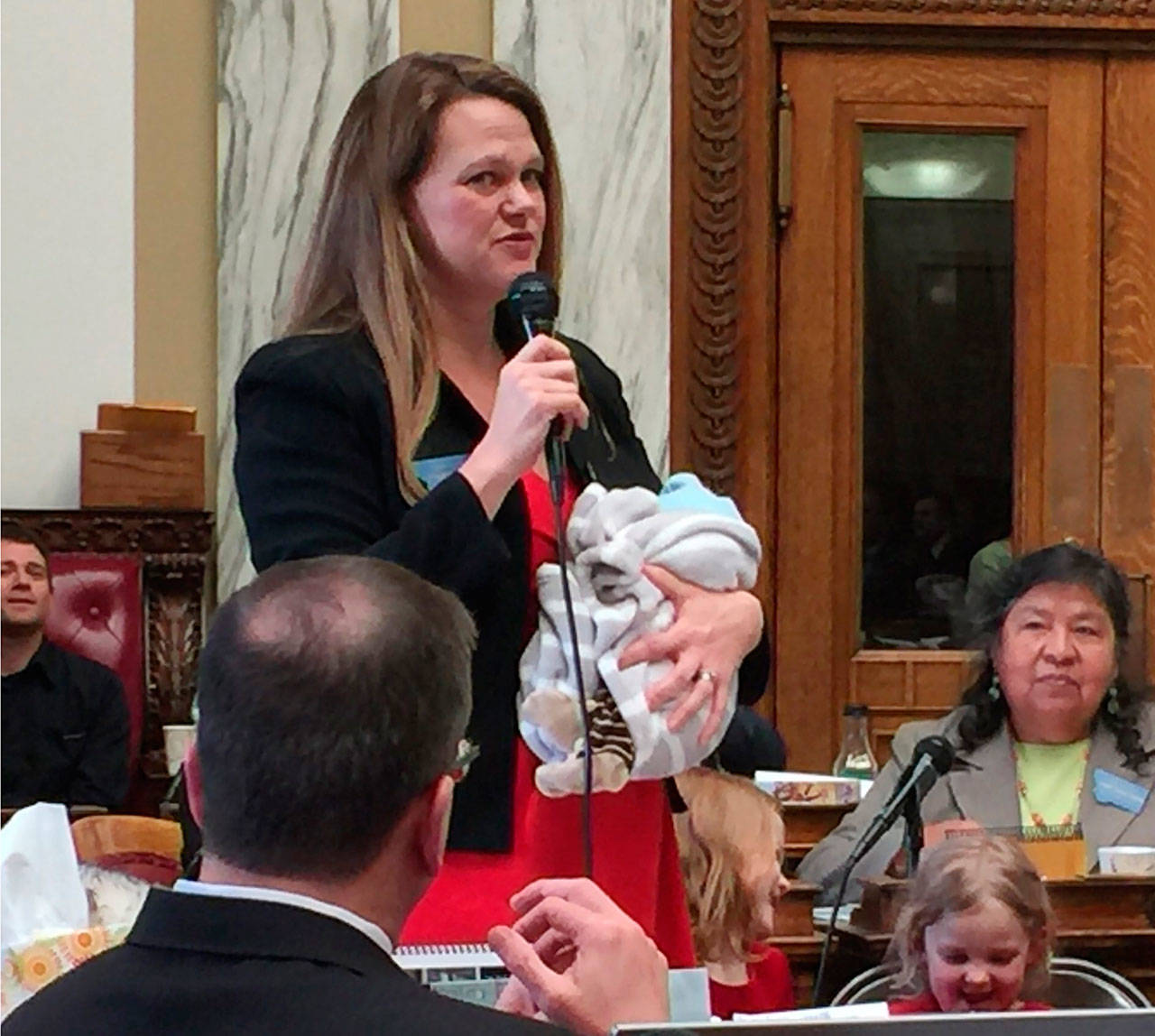 Rep. Kimberly Dudik speaks on the floor of the Legislature holding her newborn son, Marcutio, in Helena, Mont., in 2017. As experts predict another banner year of women running for office, hurdles remain particularly for those like Dudik who have young children. (Rep. Nate McConnell/Rep. Kimberly Dudik via AP)