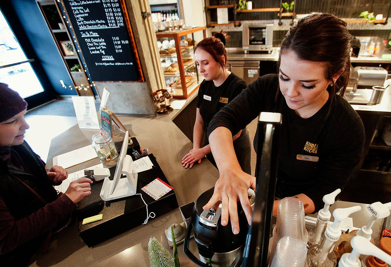 Makenna Chapman (center) helps customers at the cash register while barista Faith Littlefield (right) prepares coffee at Kindred Kitchen. (Dan Bates / The Herald)