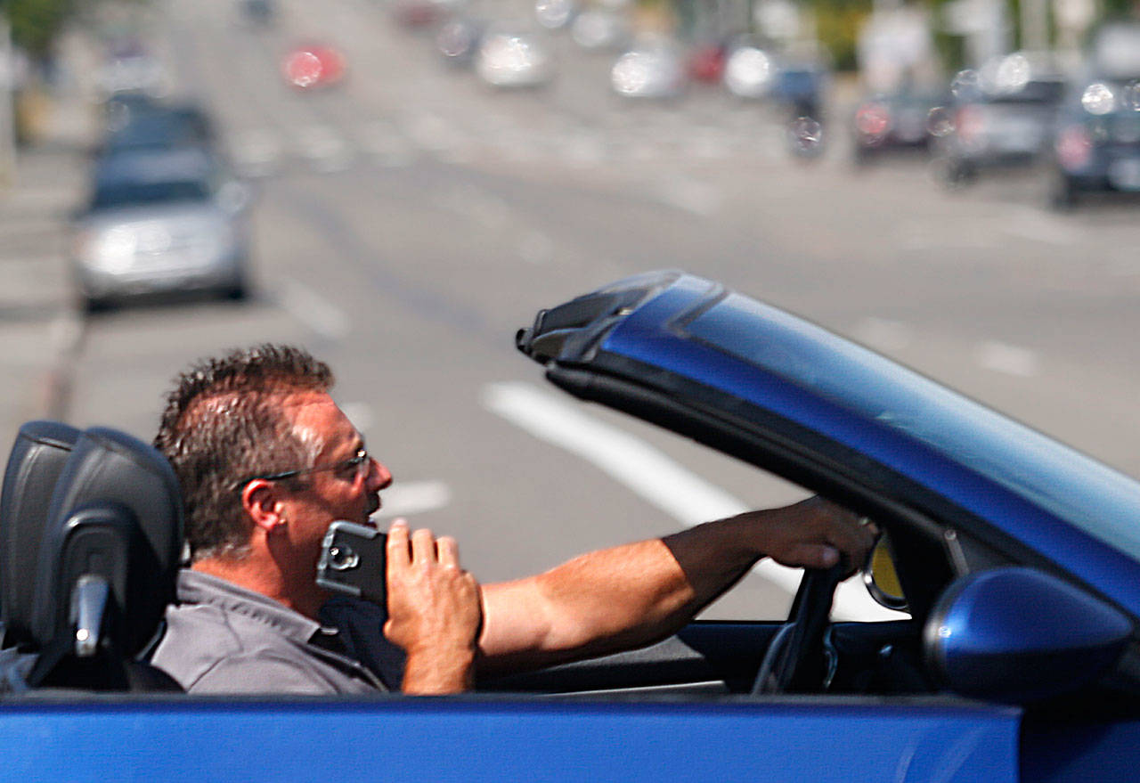 The driver of a BMW convertible appears to be talking on a cell phone while driving through the 41st Street and Colby Avenue intersection July 22, 2015. Doing so is illegal and dangerous, but is becoming less common. (Dan Bates / Herald file)