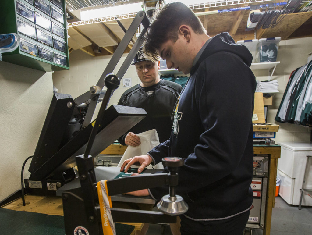 Everett Silvertips equipment manager James Stucky (rear) and his son, C.J. Stucky work on the nameplate for a new member of the team on Jan. 7 at Angel of the Winds Arena in Everett. C.J. Stucky plays for the Jr. Silvertips 18U team. (Olivia Vanni / The Herald).
