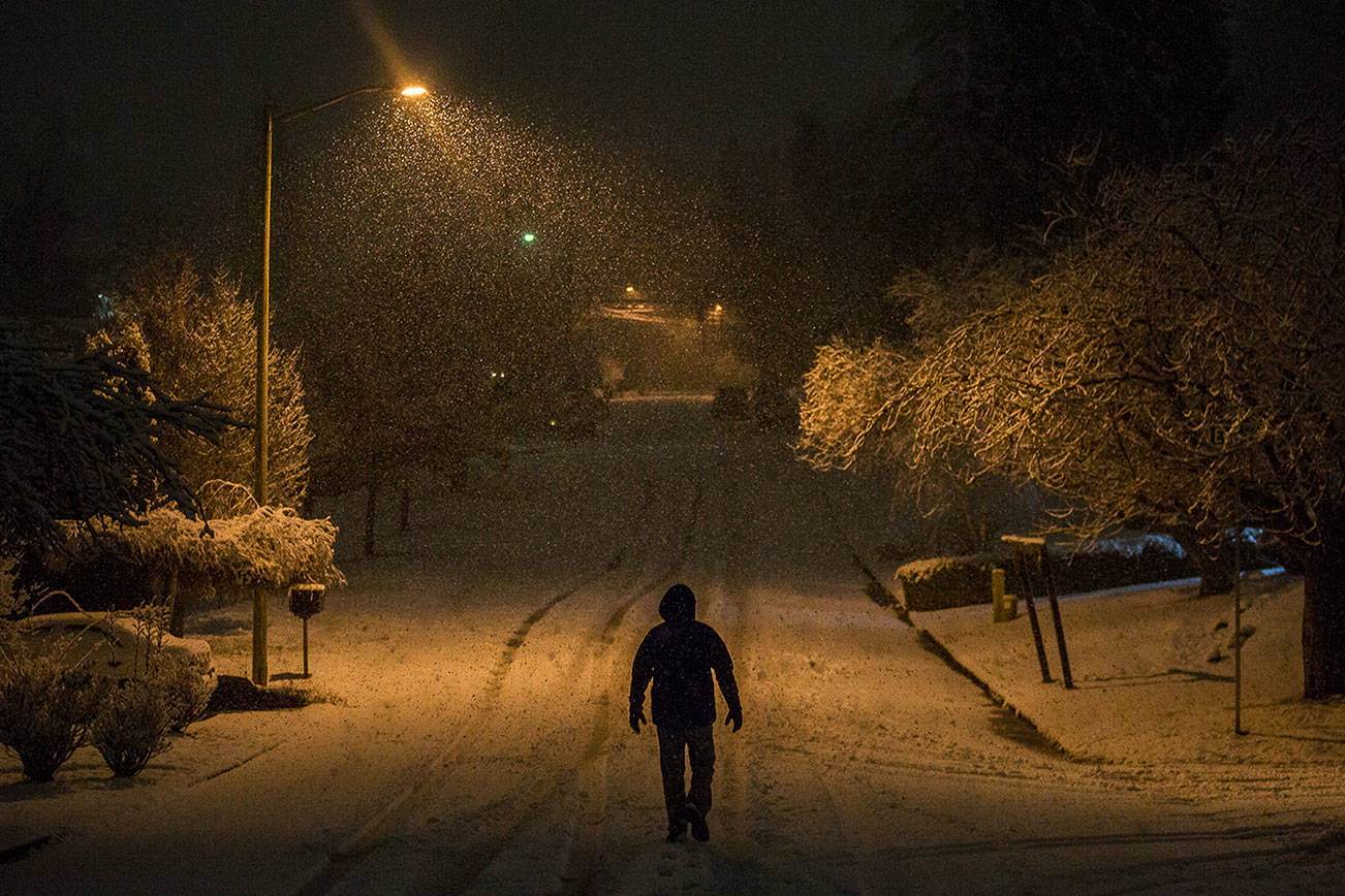 A man makes his way down View Ridge Drive as snow continues to fall on Sunday evening in Everett, Wash. (Olivia Vanni / The Herald).