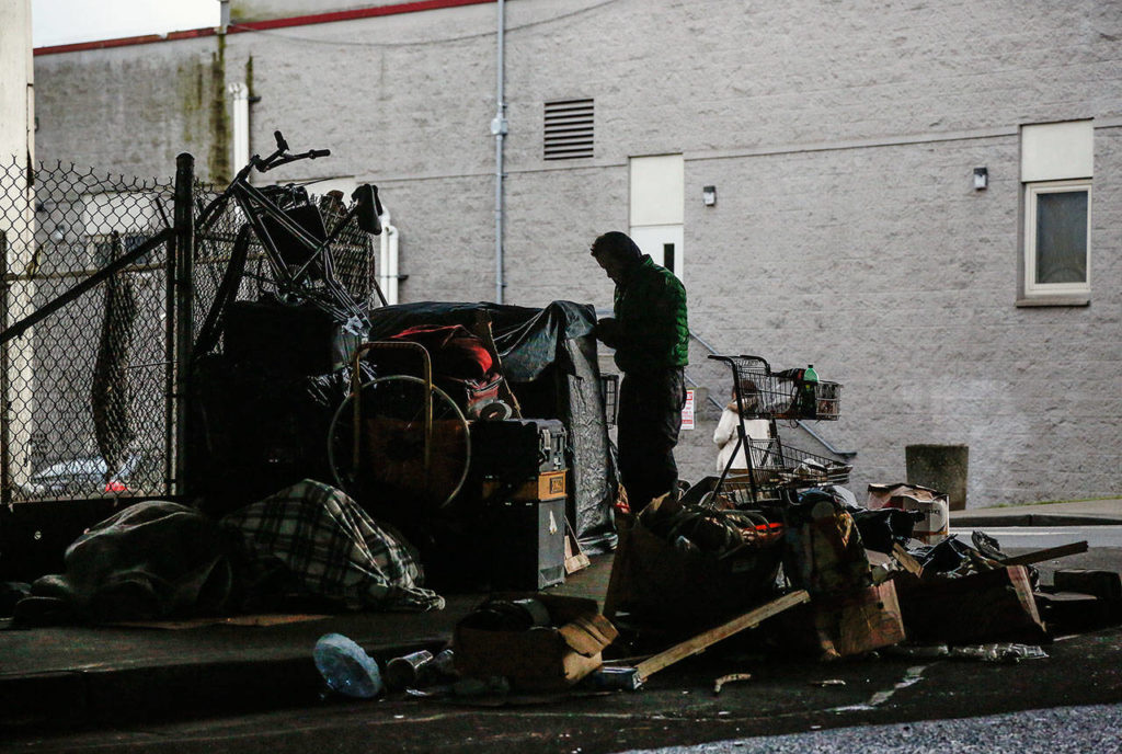 A man secures tarps over personal belongings beneath Interstate 5 overpass next to the Everett Gospel Mission, Tuesday. (Dan Bates / The Herald)
