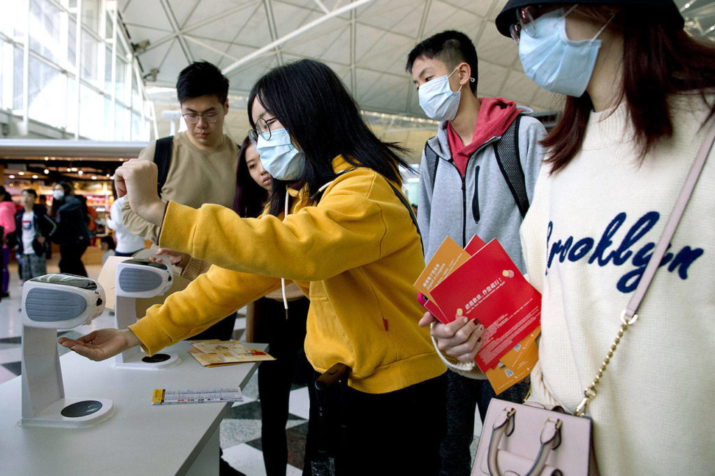 Travelers wearing face masks gather at Hong Kong International Airport on Tuesday to get squirts of antibacterial lotion after the outbreak of a new coronavirus that has reached Snohomish County — the first confirmed case in the U.S. (AP Photo/Ng Han Guan)
