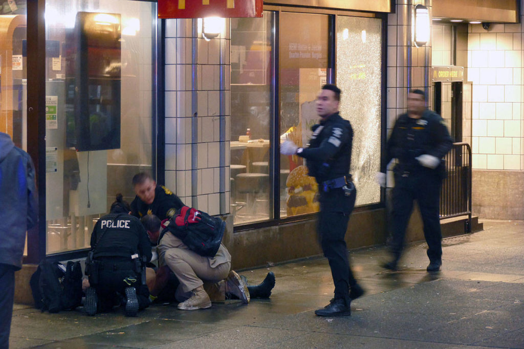 Officers attend to one of several shooting victims outside of McDonald’s on Third Avenue on Wednesday in Seattle. The window of the restaurant behind them was shattered after a gunman opened fire in the heavily trafficked downtown area. (David Silver via AP)
