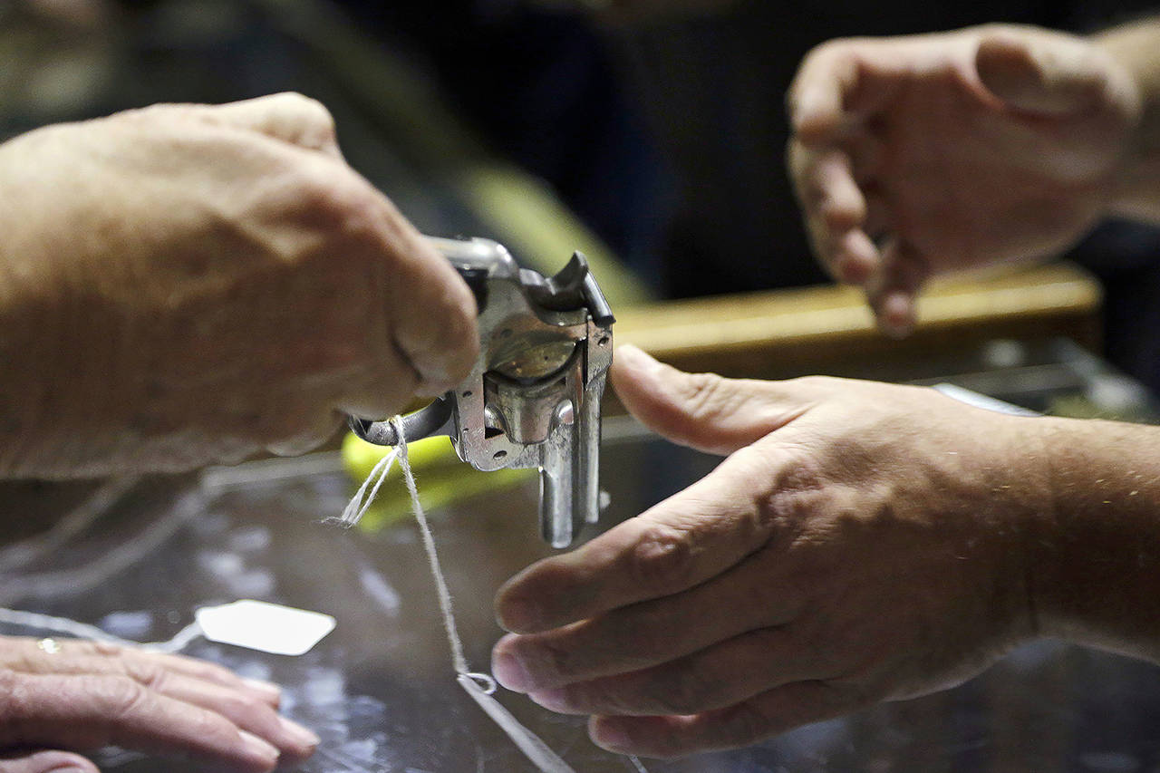 In this 2017 photo, a sales clerk hands a pistol, being sold on behalf of the Aberdeen Police Department, to a customer to look at before an auction at Johnny’s Auction House, where the company handles gun sales for police departments and the Lewis County Sheriff’s Office, in Rochester, Washington. (AP Photo/Elaine Thompson, File)