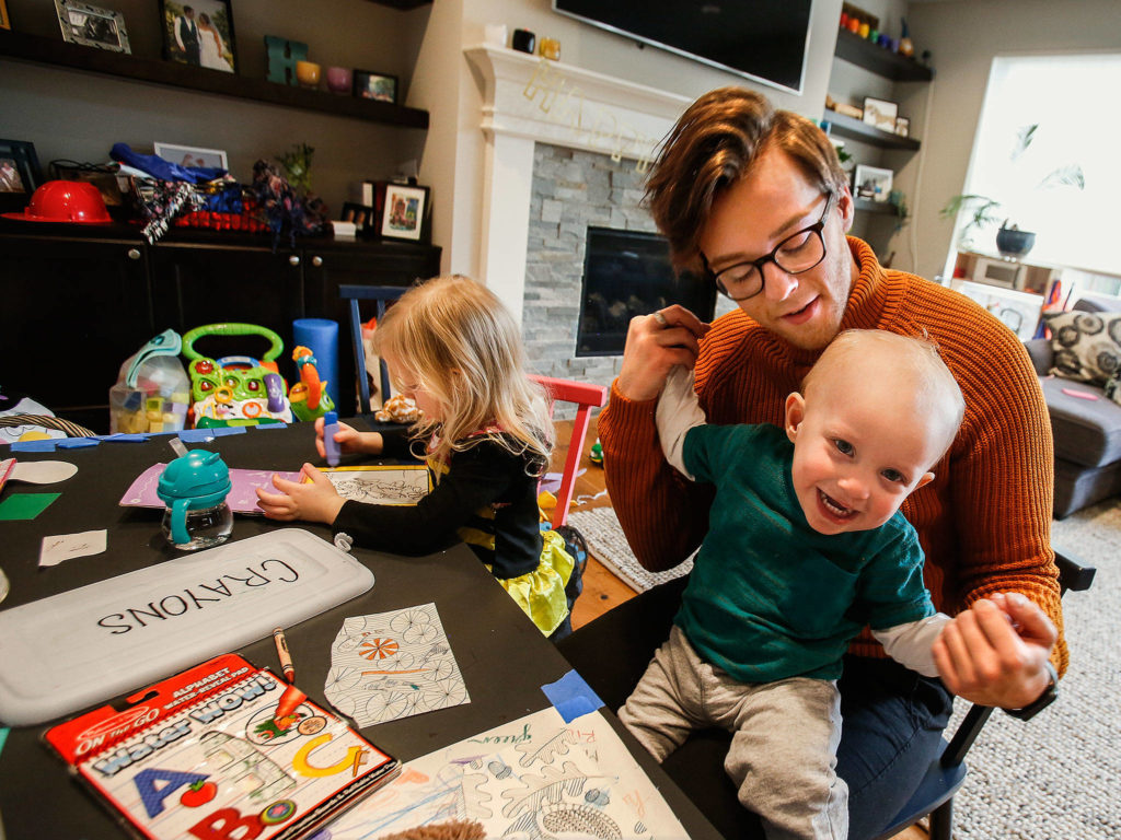 Rico Baumgardt, a 21-year-old au pair from Germany, plays with year-old Owen Hertl as Owen’s sister, Bianca, 4, creates artwork at a kid-size table in the Hertl family’s Edmonds home Monday. Next month, Baumgardt will return home after a year with the family. (Dan Bates / The Herald)
