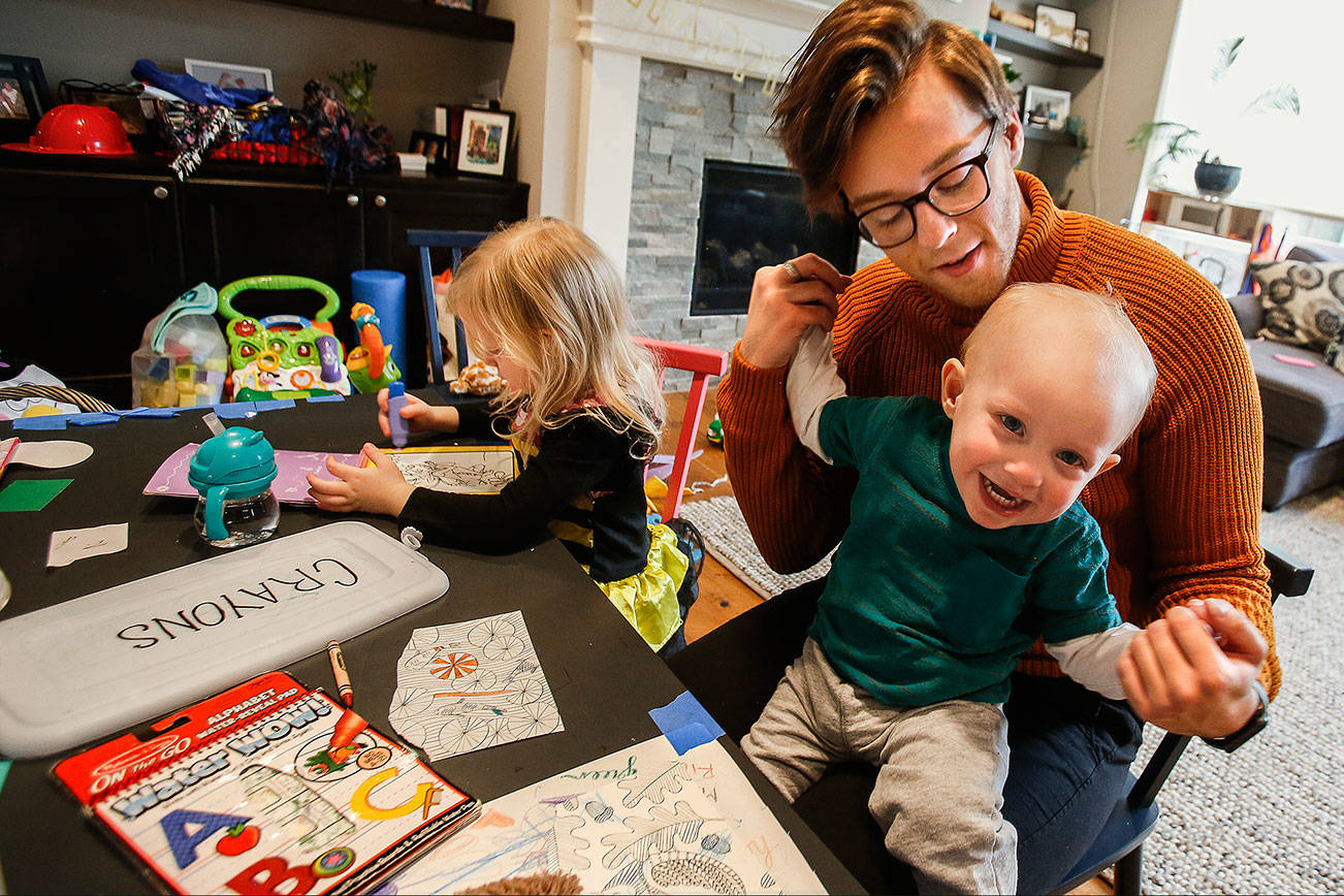 Rico Baumgardt, a 21-year-old au pair from Germany, plays with year-old Owen Hertl as Owen’s sister, Bianca, 4, creates artwork at a kid-size table in the Hertl family’s Edmonds home Monday. Next month, Baumgardt will return home after a year with the family. (Dan Bates / The Herald)