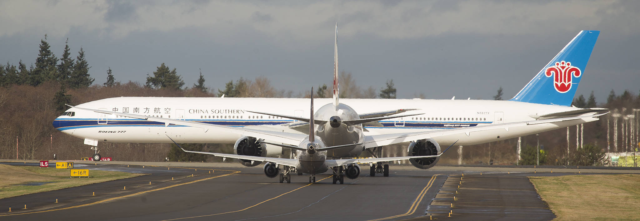 A China Southern 777-300ER, one of Boeing’s biggest airplanes, passes in front of two smaller jets, including a Boeing 787, at Paine Field last Friday in Everett. Boeing is rethinking earlier plans to offer a new mid-sized airplane, which would have served a niche just under the capacity of the 787. (Andy Bronson / The Herald)