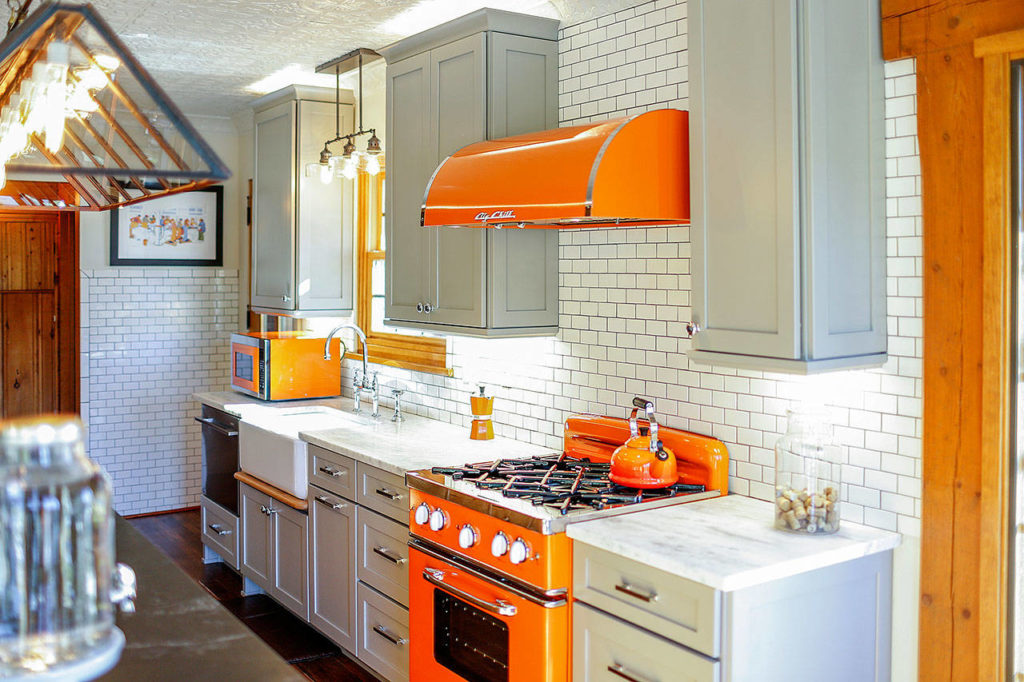 An Evergreen, Colorado, kitchen uses bright orange Big Chill appliances — the microwave, stove and range hood — to contrast more neutral cabinetry. (Brand Viva)
