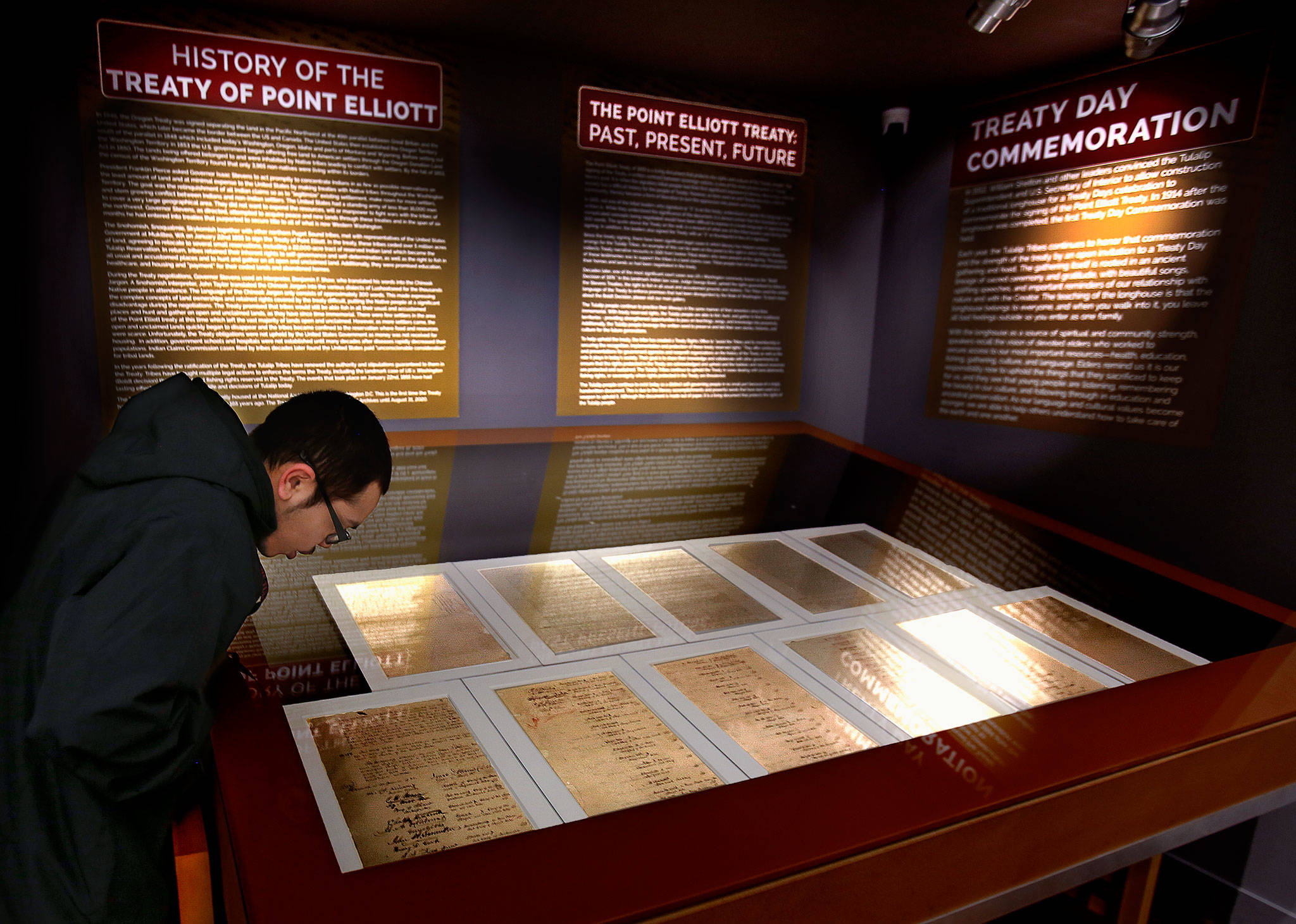 Security guard Jakeb Conway leans forward to read a piece of history on the Treaty of Point Elliott at the Hibulb Cultural Center. The large glass-covered case displays the signed documents for reading. (Dan Bates / The Herald)
