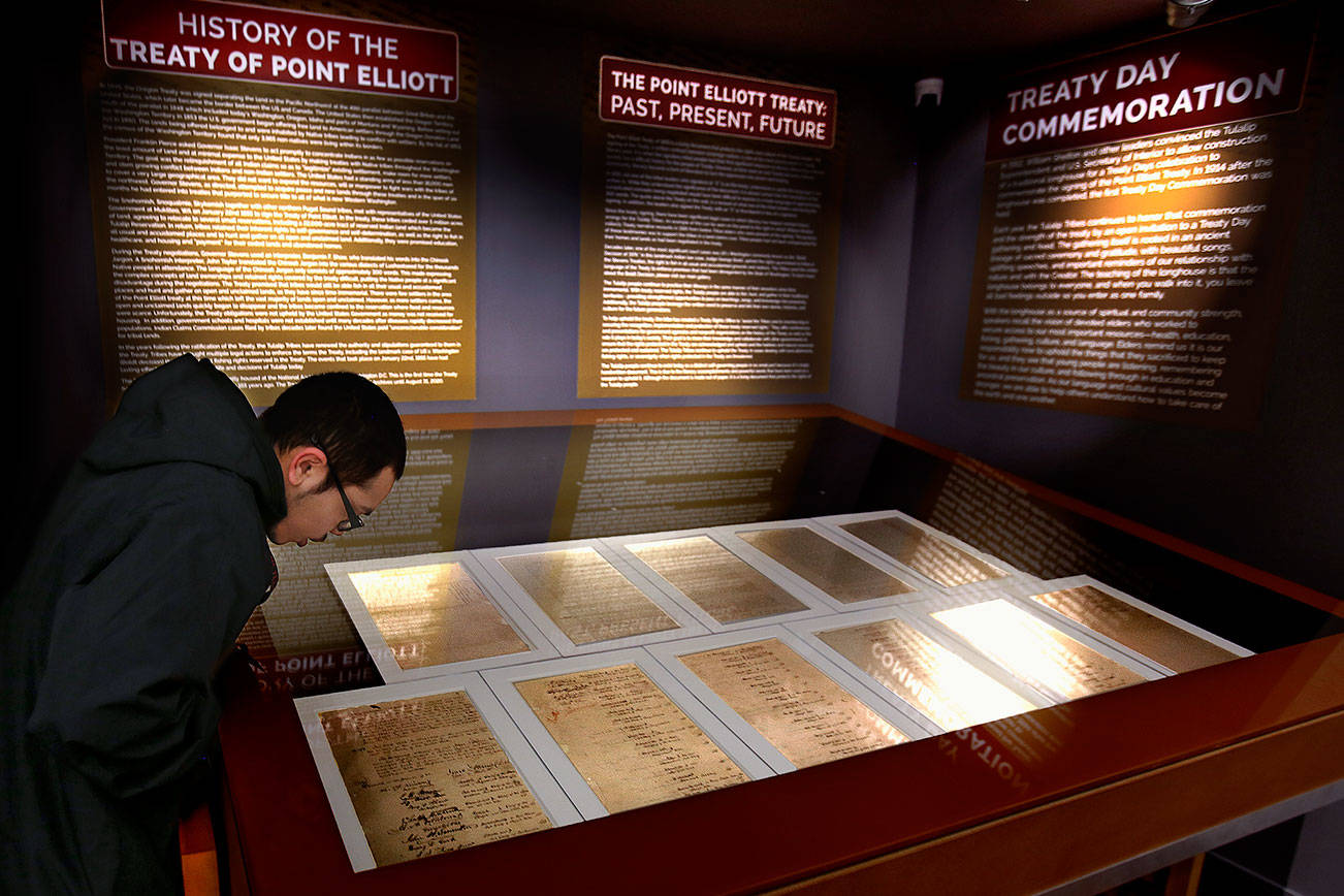 Security guard Jakeb Conway leans forward to read a piece of history on the Treaty of Point Elliott at the Hibulb Cultural Center. The large glass-covered case, center, displays the signed documents for reading. (Dan Bates / The Herald)