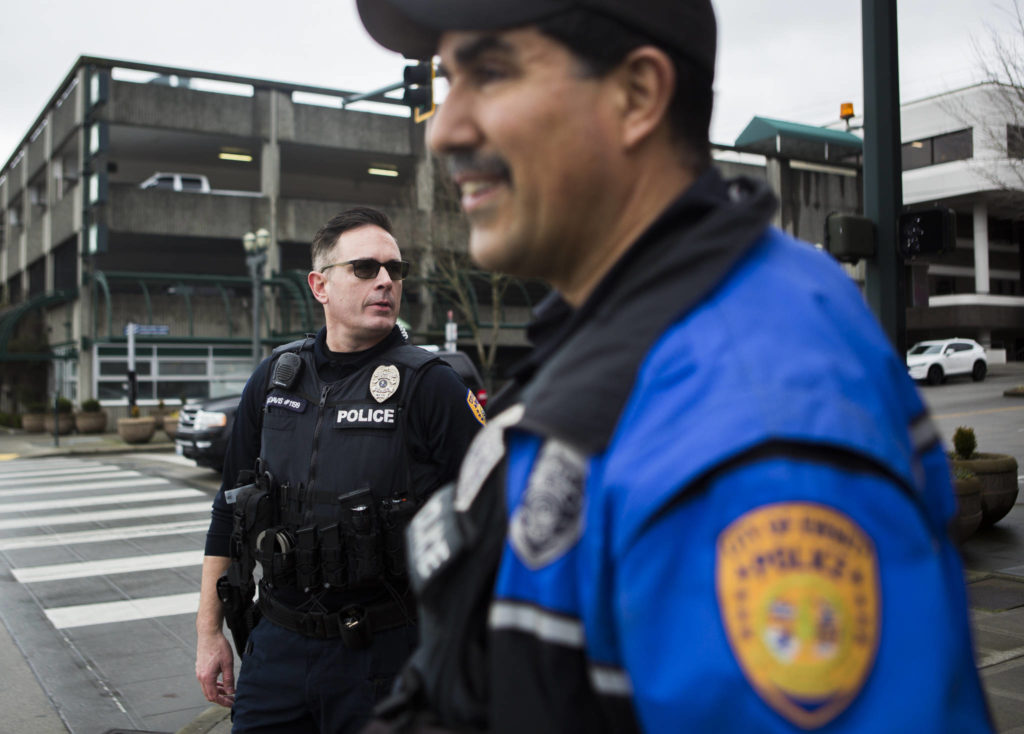 Everett Police officers Kevin Davis (left) and Mike Bernardi wait for the light to change at the corner of Hewitt and Hoyt avenues on Thursday in downtown. Everett’s mayor and police chief plan to hire 24 additional officers by 2023 to bolster the department’s visible presence in the community. (Olivia Vanni / The Herald)
