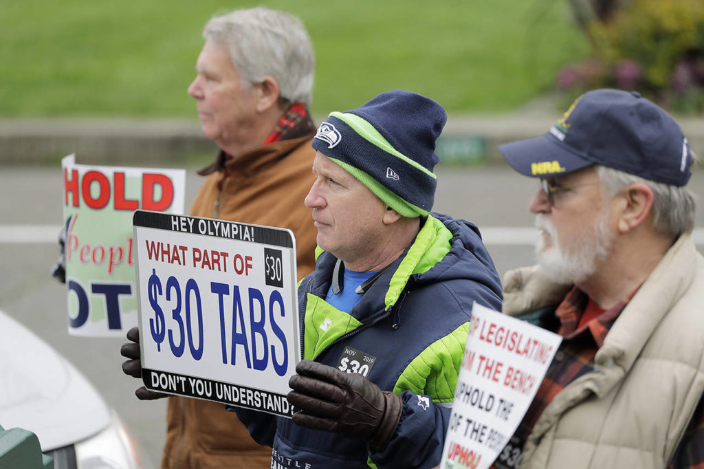Dan Cockerham (center) of Puyallup, holds a sign that reads “Hey Olympia, what part of $30 car tabs don’t you understand?” on Jan. 13, as he attends a rally on the first day of the 2020 session of the Washington legislature, at the Capitol in Olympia. (AP Photo/Ted S. Warren)
