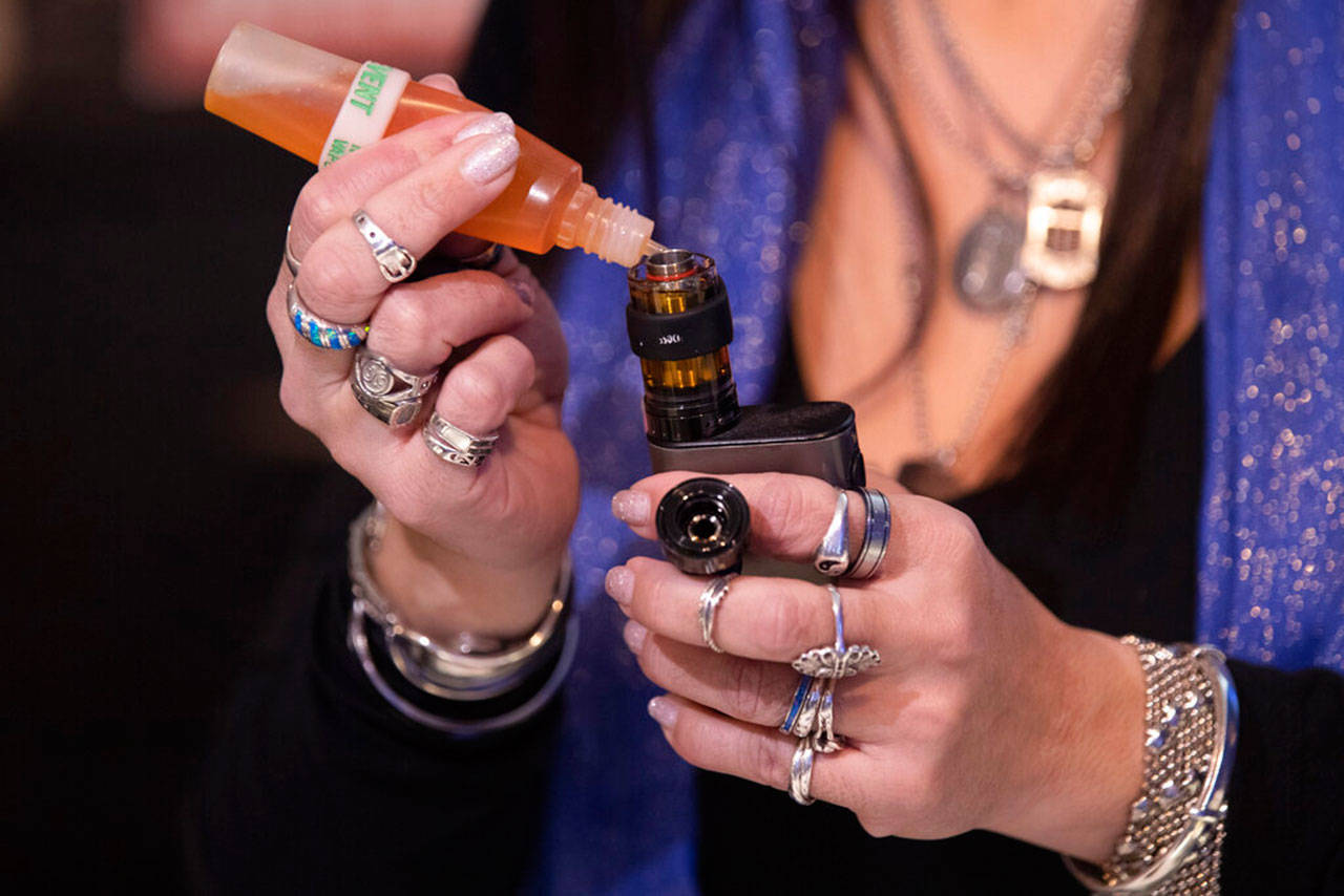 Spike Babaian, owner of the VapeNY.com store refills her vaping device with a flavored liquid, Jan. 2, 2020, in New York. U.S. health officials will ban most flavored e-cigarettes popular with underage teenagers, but with major exceptions that benefit vaping manufacturers, retailers and adults who use the nicotine-emitting devices. (Mary Altaffer / Associated Press)