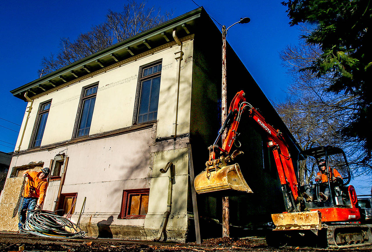 Outside the Snohomish Carnegie Library, contractor Rob Enge (left) attaches a chain to a roll of heavy cable as Kody Brooks approaches to help carry it with a tractor Tuesday at one side of the original building as it begins to look more and more like it did before an annex was added in the 1960s. (Dan Bates / The Herald)