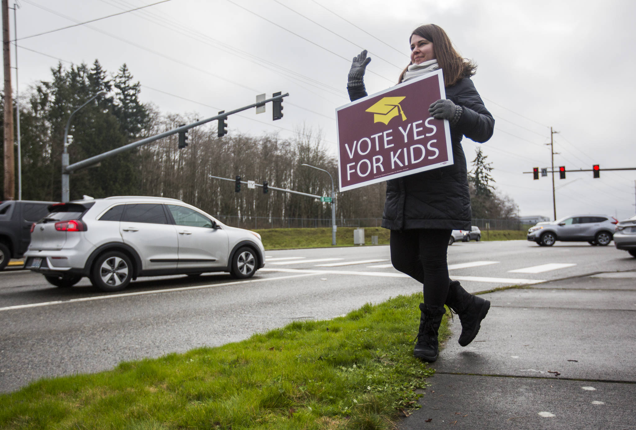 Jaime Benedict, who works as a substitute teacher, waves to drivers Tuesday at the corner of Mukilteo Speedway and Harbor Pointe Boulevard while holding a sign in support of the $240 million capital bond proposal for the Mukilteo School District. (Olivia Vanni / The Herald)