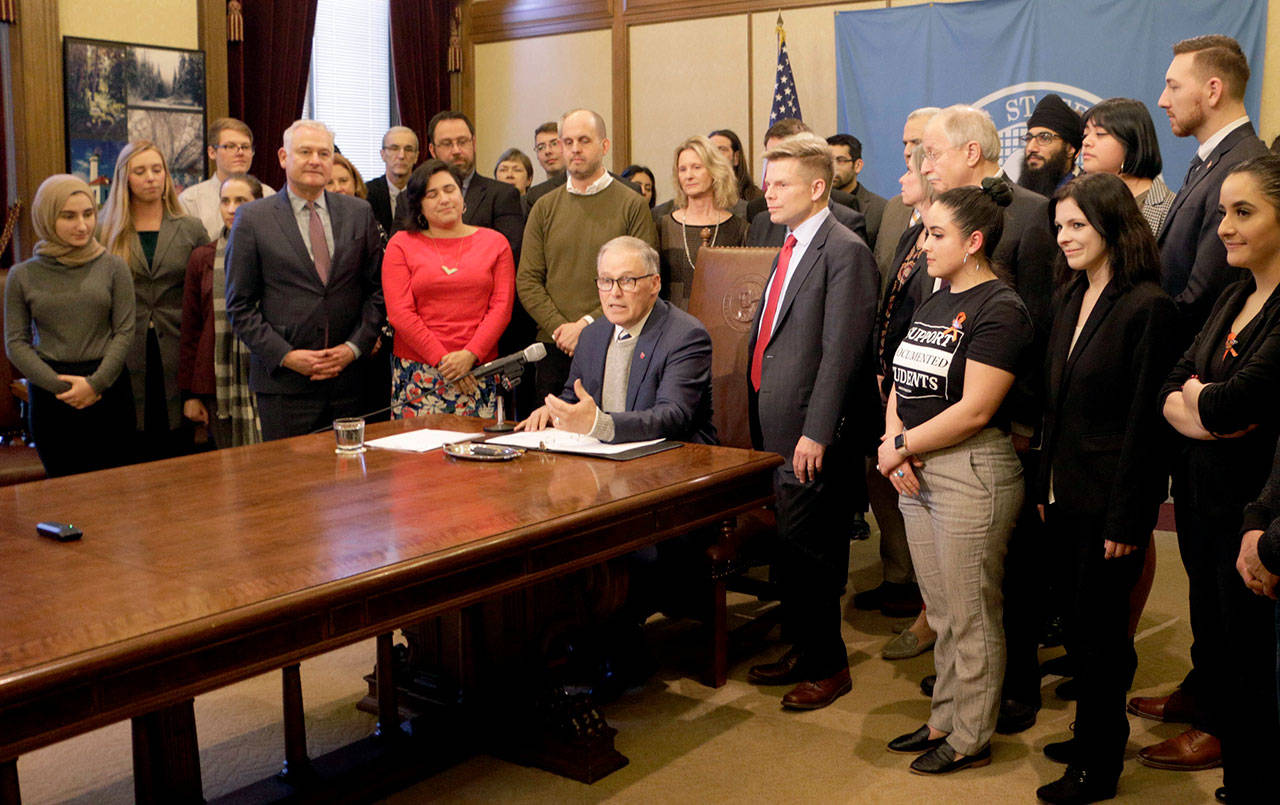 Washington Gov. Jay Inslee (seated) is surrounded by lawmakers and supporters of a college grant program he signed into law Monday in Olympia. (AP Photo/Rachel La Corte)