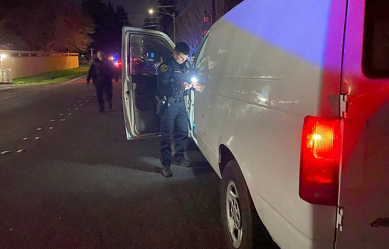 A Lynnwood Police Department officer inspects a van Monday night after its driver allegedly struck a woman riding her bike on 176th Street SW. near 60th Avenue W., in Lynnwood. (Lynnwood Police Department)