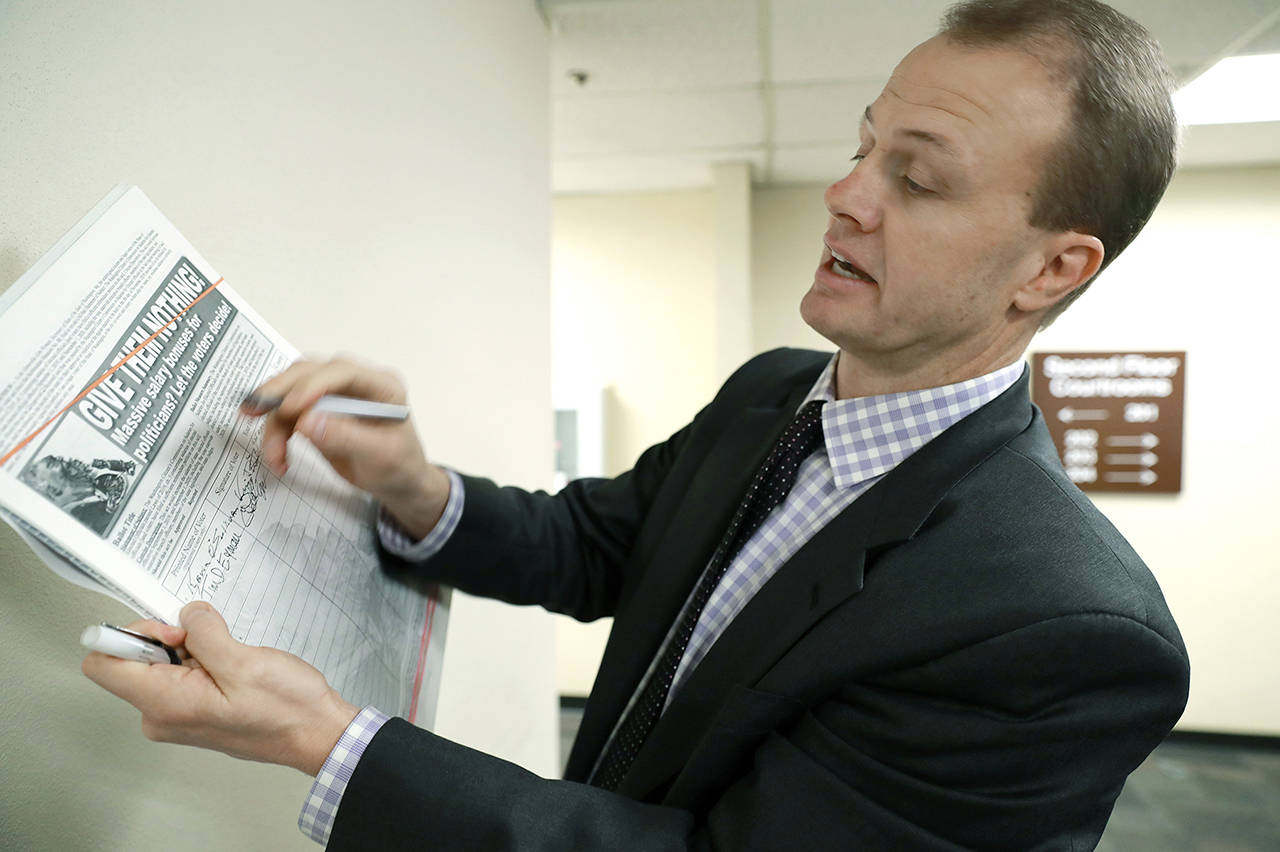 This 2019 photo shows Tim Eyman signing his initiative that would limit pay raises for elected officials, following his appearance in Thurston County Superior Court in Olympia. (Associated Press file)