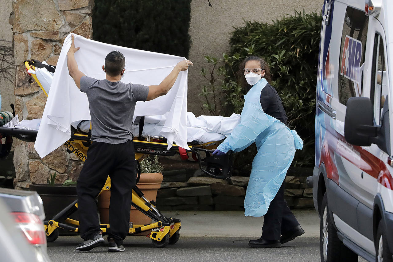A staff member blocks the view as a person is taken by a stretcher to a waiting ambulance from a nursing facility where more than 50 people are sick and being tested for the COVID-19 virus, Saturday in Kirkland. Health officials reported two cases of COVID-19 virus connected to the Life Care Center of Kirkland. (AP Photo/Elaine Thompson)