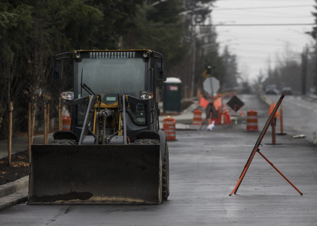 A loader truck and construction sign sit along 36th Avenue West in Lynnwood. The road is under construction and nearing completion. (Olivia Vanni / The Herald)
