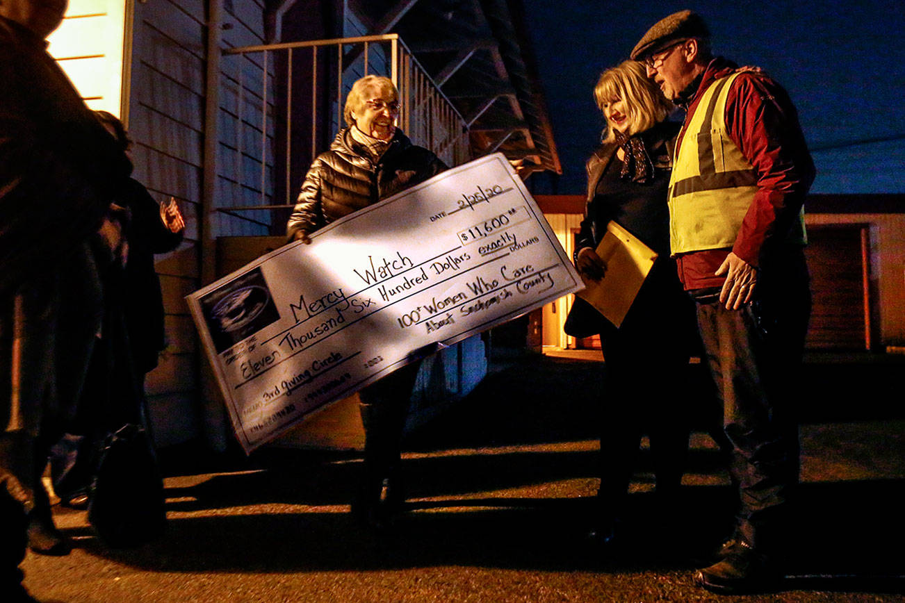 Dennis Kelly, of Mercy Watch, is wowed by a donation of $11,600 from 100+ Women Who Care About Snohomish County. In the parking lot of Everett’s Our Lady of Perpetual Help Church Tuesday, Sue Rieke presents the symbolic check while Janet Bacon, the women’s group founder, and Kelly talk about the donation. (Dan Bates / Herald Photographer)