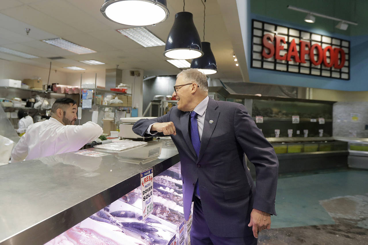 Washington Gov. Jay Inslee (right) bumps elbows with a worker at the seafood counter of the Uwajimaya Asian Food and Gift Market on Tuesday in Seattle’s International District. Inslee said he’s doing the elbow bump with people instead of shaking hands to prevent the spread of germs, and that his visit to the store was to encourage people to keep patronizing businesses during the COVID-19 Coronavirus outbreak. (AP Photo/Ted S. Warren)