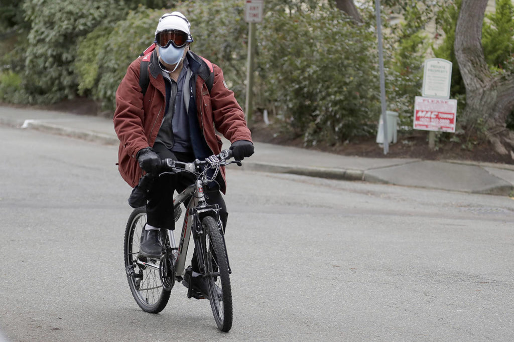 Ted S. Warren / Associated Press
A man wearing a mask and goggles rides his bike out of the parking lot at the Life Care Center in Kirkland on Tuesday. The facility has been tied to several confirmed cases of the COVID-19 coronavirus.
