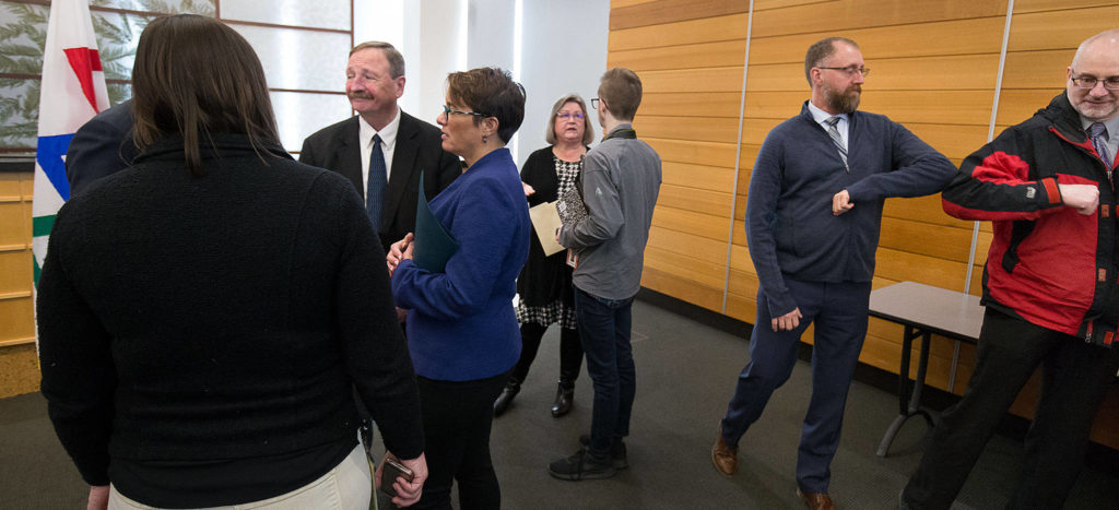 After a news conference, where officials issued new recommendations for limiting the spread of the COVID-19 virus, Snohomish County Emergency Management Director Jason Biermann and City of Monroe Public Works Director Brad Fielberg touch elbows before leaving the room on Thursday in Everett. (Andy Bronson / The Herald)
