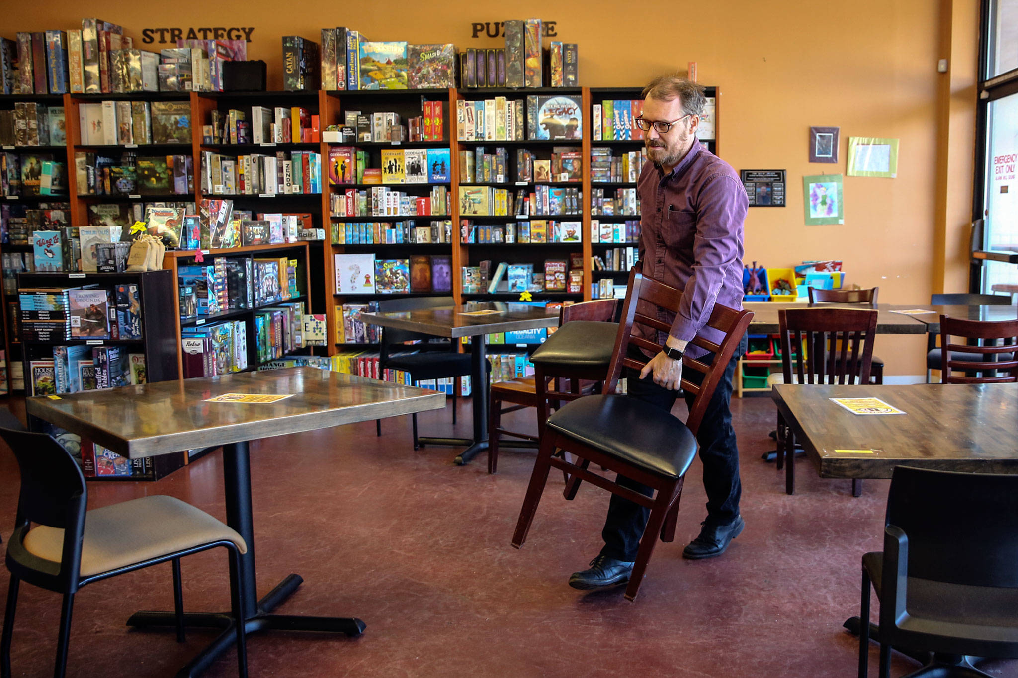 Tim Morgan, co-owner, removes chairs to conform to then-new health policies March 15 at Around the Table Game Pub in Lynnwood. (Kevin Clark / The Herald)