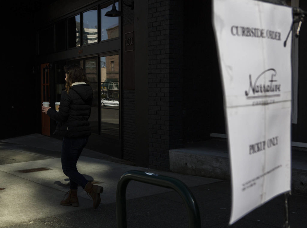 Narrative Coffee employee Eugenia Nestico walks down the sidewalk past a pickup only sign to deliver coffee to customers on Thursday in Everett. (Olivia Vanni / The Herald)
