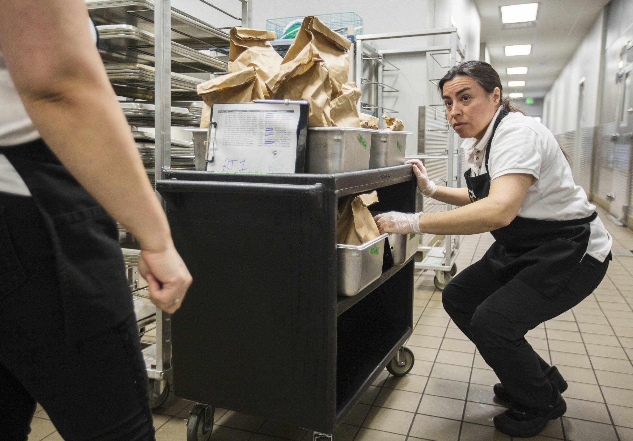 Ileana Koons organizes vegetable and meat meal options as the kitchen prepares food Thursday at North Creek High School in Bothell. (Olivia Vanni / The Herald)