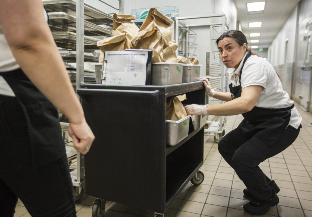 Ileana Koons organizes vegetable and meat meal options as the kitchen prepares food Thursday at North Creek High School in Bothell. (Olivia Vanni / The Herald)
