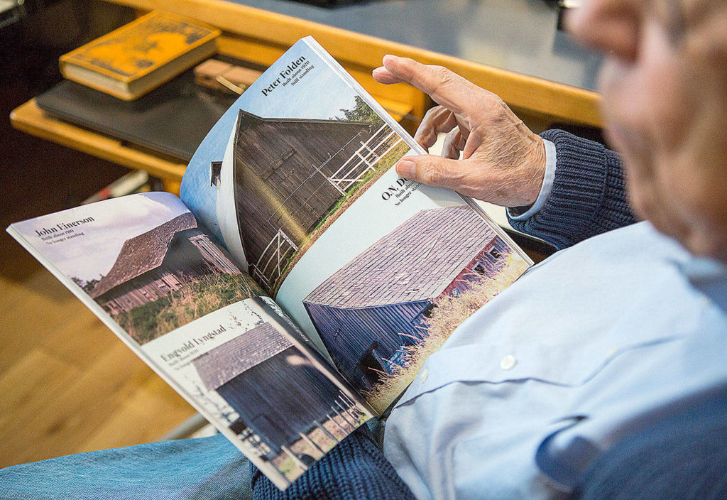 Gerald Magelssen pages through his book of Camano Island barn photographs. (Olivia Vanni / The Herald)
