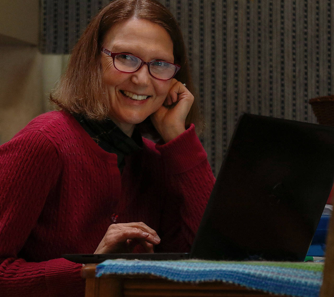 Herald columnist Julie Muhlstein appears to be happy while working at her kitchen table Tuesday, but finds that doing her job from her north Everett home has its challenges. (Dan Bates / The Herald)