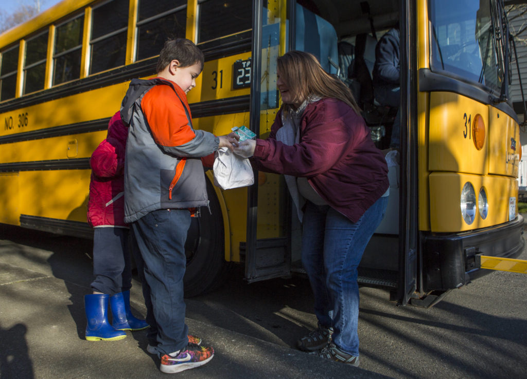 Amber Moore (right) hands Lincoln Ruiz, 8, a breakfast and lunch during their meal delivery at Carroll’s Creek neighborhood on Wednesday in Marysville. (Olivia Vanni / The Herald)
